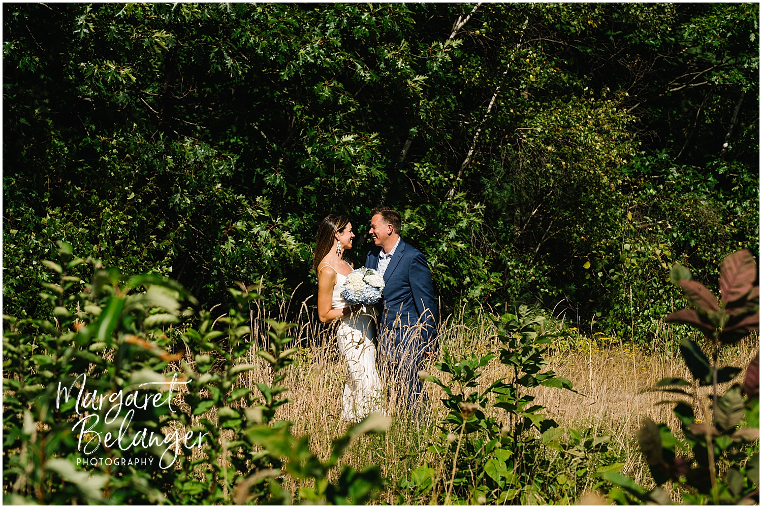 Bride and groom sharing a moment in a sunny meadow with greenery in the background.