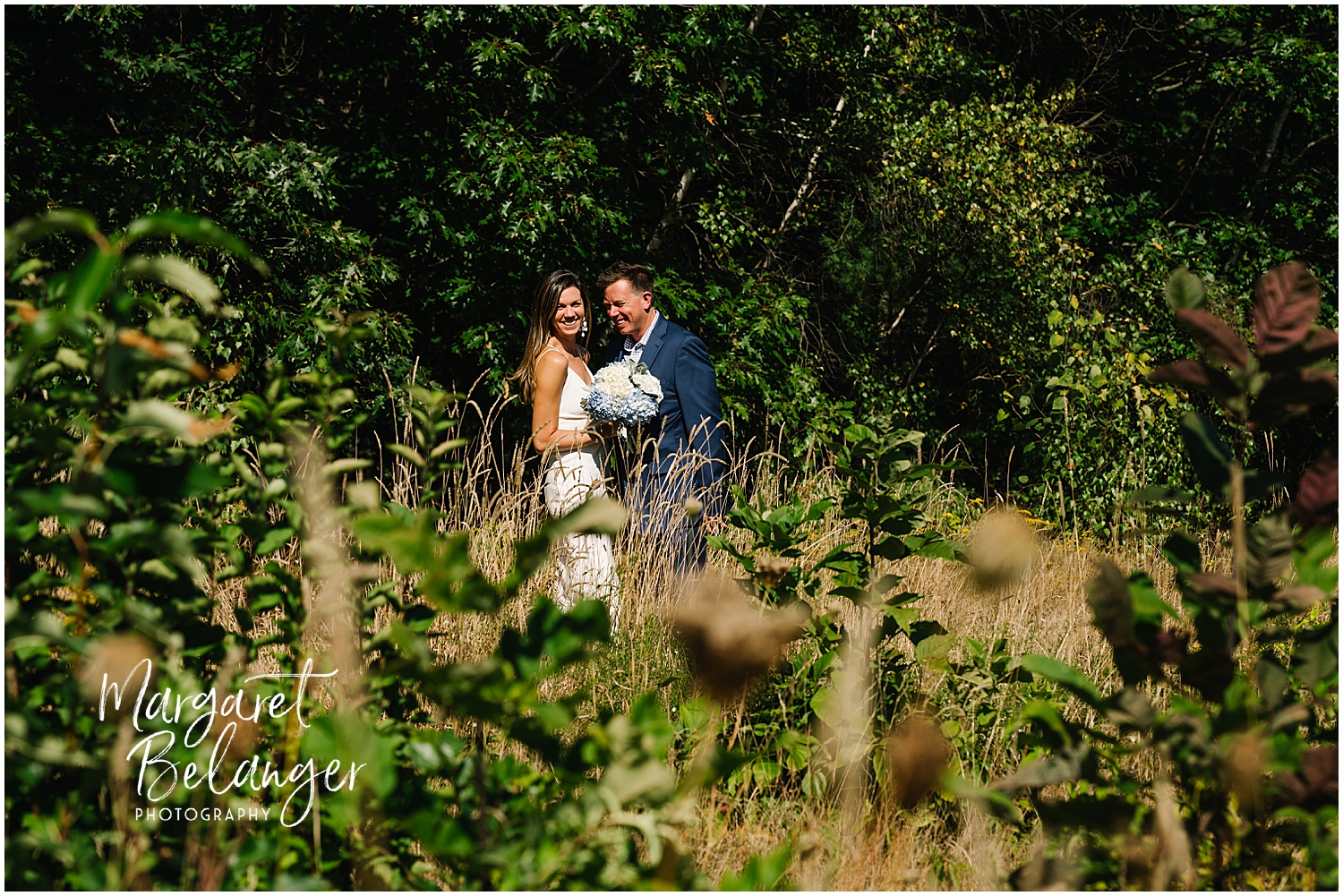 Couple in wedding attire sharing a funny moment amidst lush greenery.