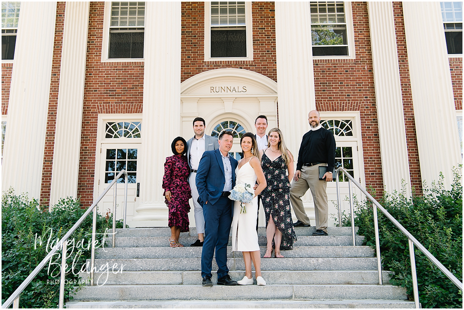 A bride and groom and their five wedding guests posing on the steps of a building named "Runnals".