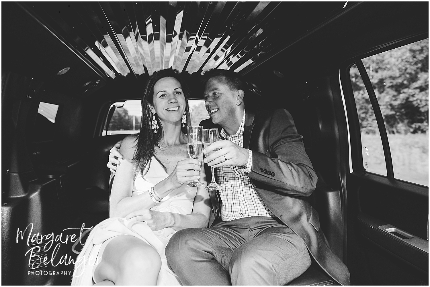 A bride and groom toasting with champagne inside a limousine while the bride looks at the camera and the groom looks at the bride.
