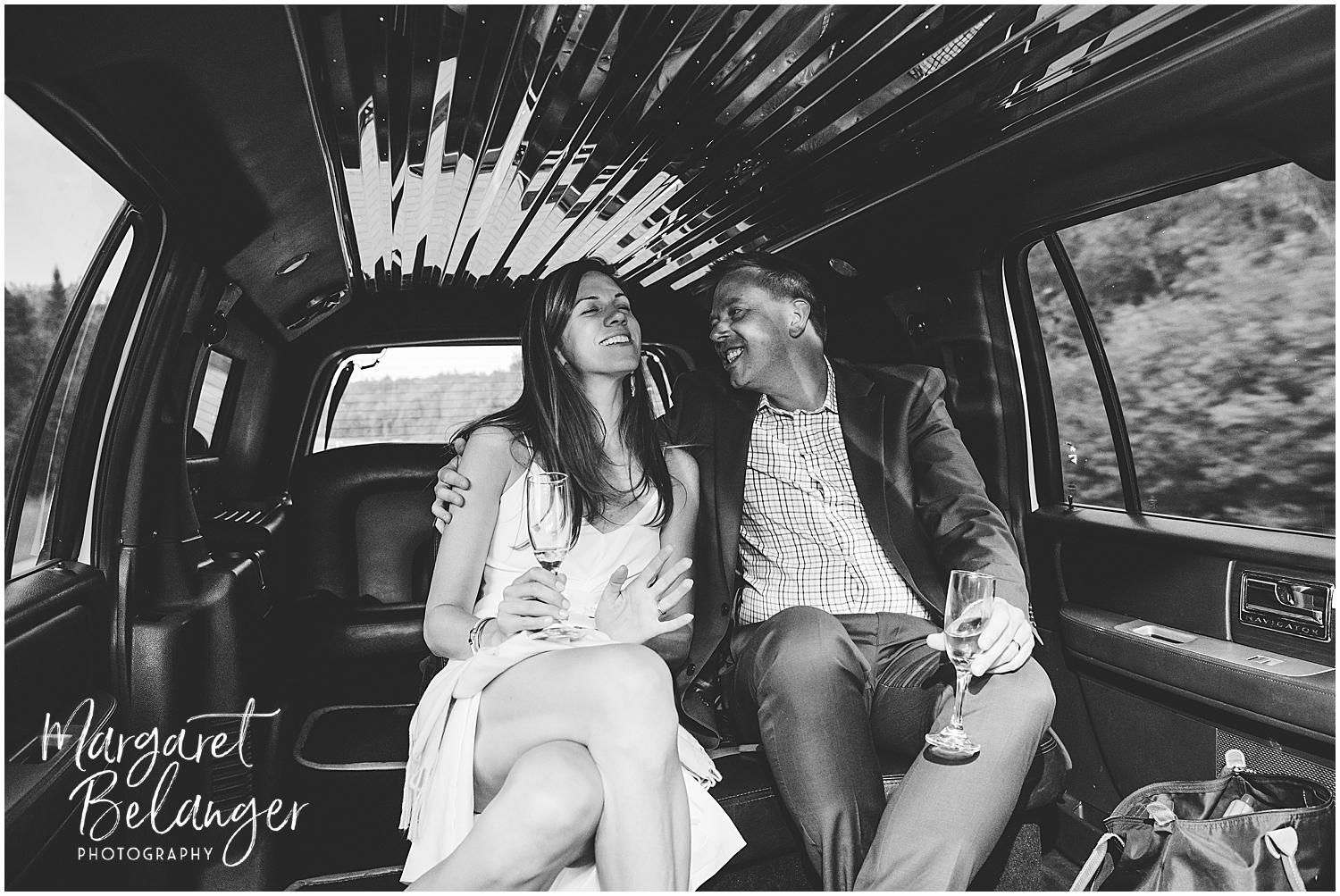 A bride and groom singing together in the back seat of a limousine with a glass of champagne.